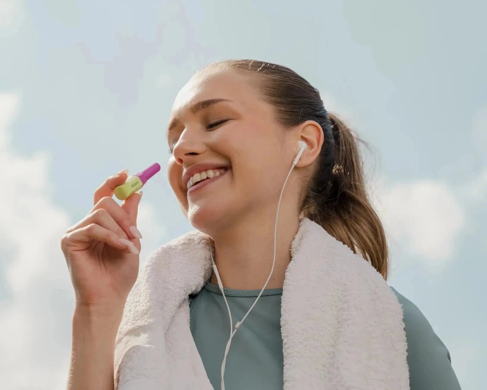 Woman with a towel around her neck, listening to music outdoors with a clear sky background